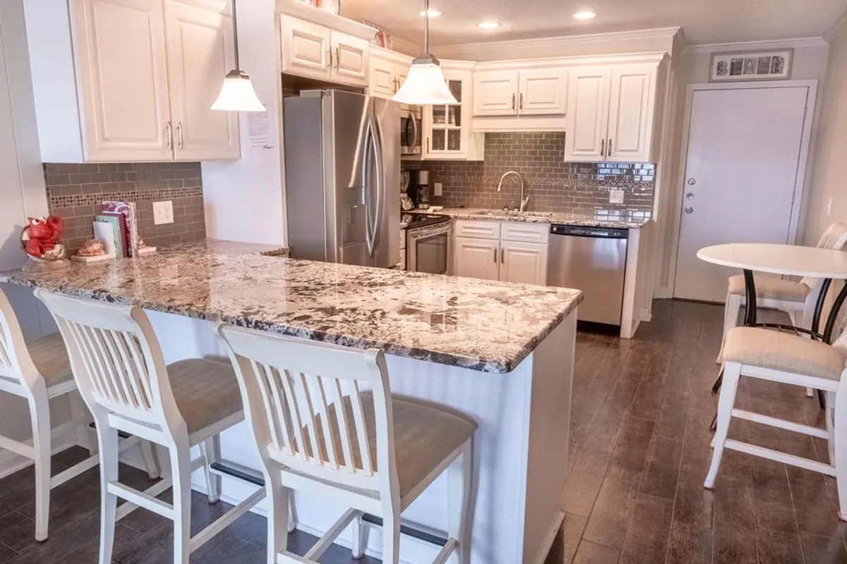 A stylish kitchen with a granite island and seating, modern appliances, and elegant lighting. The kitchen is integrated with the main living space, supporting activities like cooking, socializing, and meal preparation.