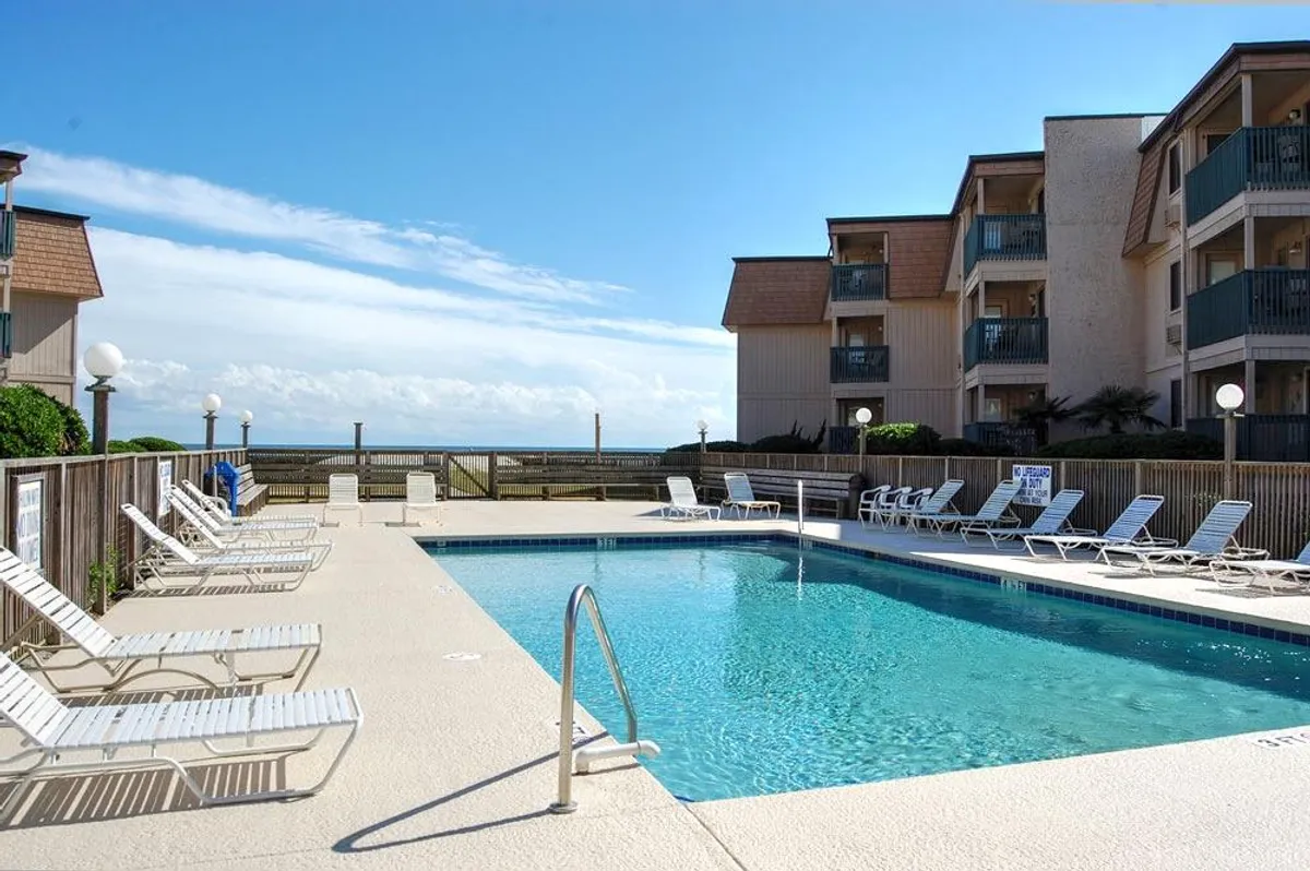 A sparkling swimming pool surrounded by lounge chairs, with the building’s balconies and a glimpse of the ocean in the background. The atmosphere is relaxing, with ample space for sunbathing or socializing by the poolside.