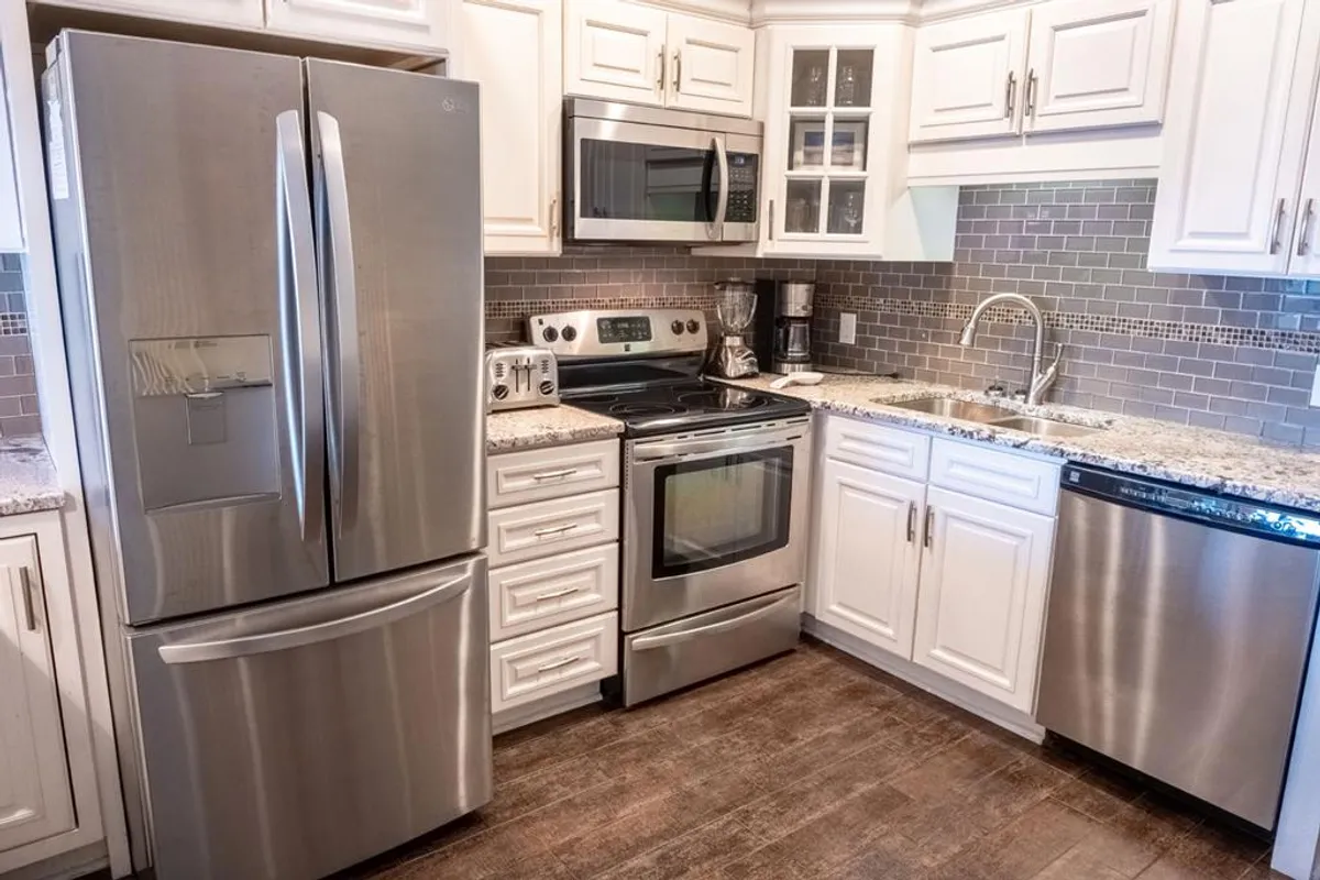 A spacious, modern kitchen featuring a stainless steel refrigerator, sleek modern stove, granite countertops, and crisp white cabinetry. The area is well-lit and arranged to facilitate both cooking and socializing, making it perfect for gathering with friends or family while preparing meals.