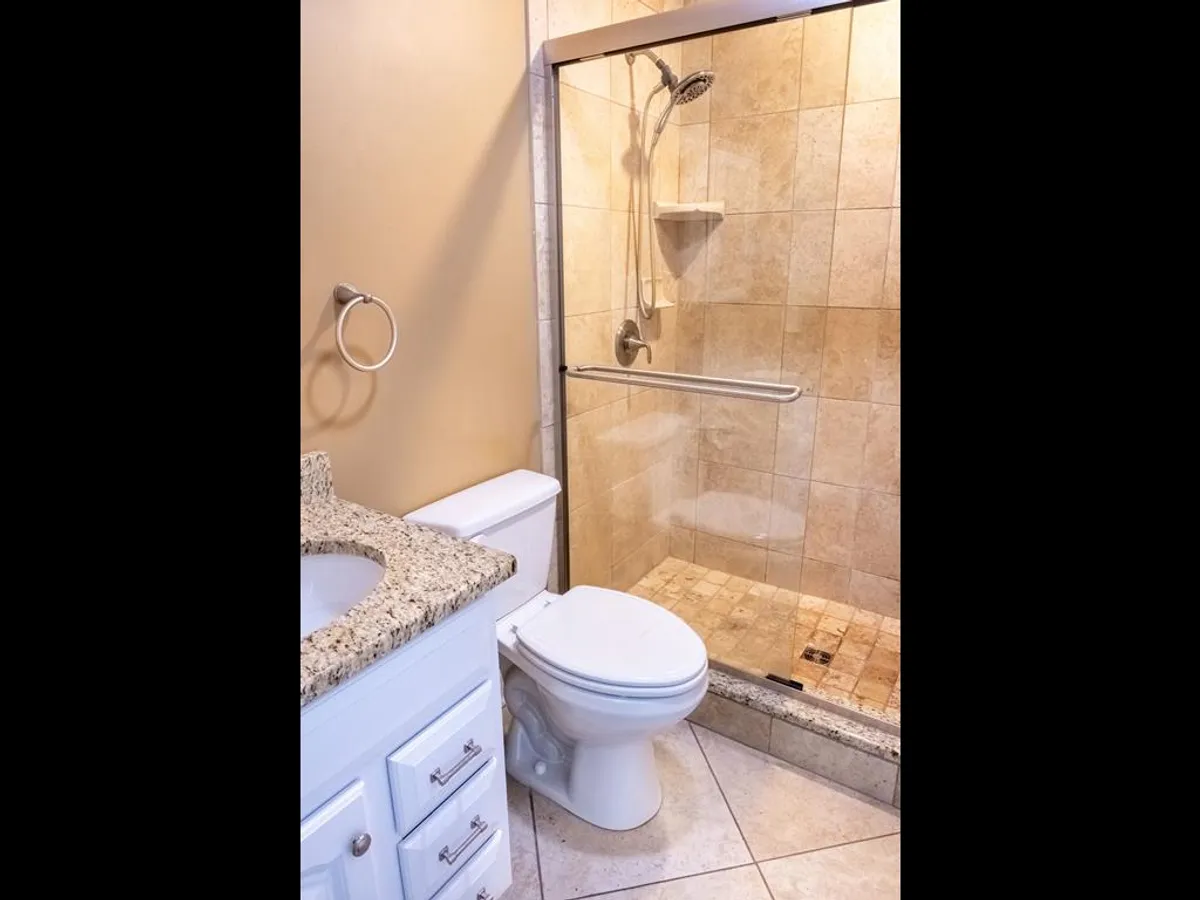 A modern bathroom with a granite countertop, glass shower enclosure, and neutral tile flooring. The space feels inviting and fresh, designed for personal care and relaxation.