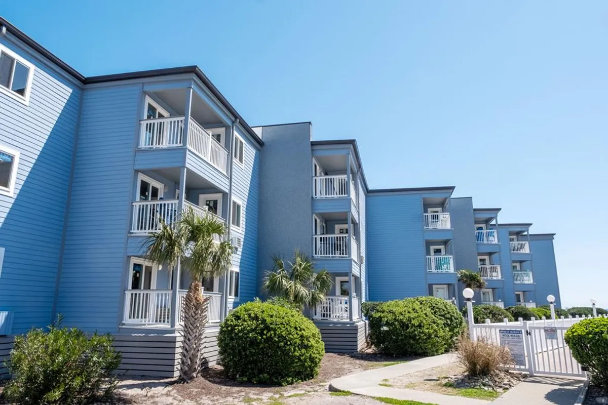 This image showcases the blue exterior of the Shore Drive condo building, featuring multiple balconies with white railings and lush greenery around the property. The balconies hint at private outdoor spaces perfect for group gatherings, and the landscaping gives a welcoming, resort-style vibe.