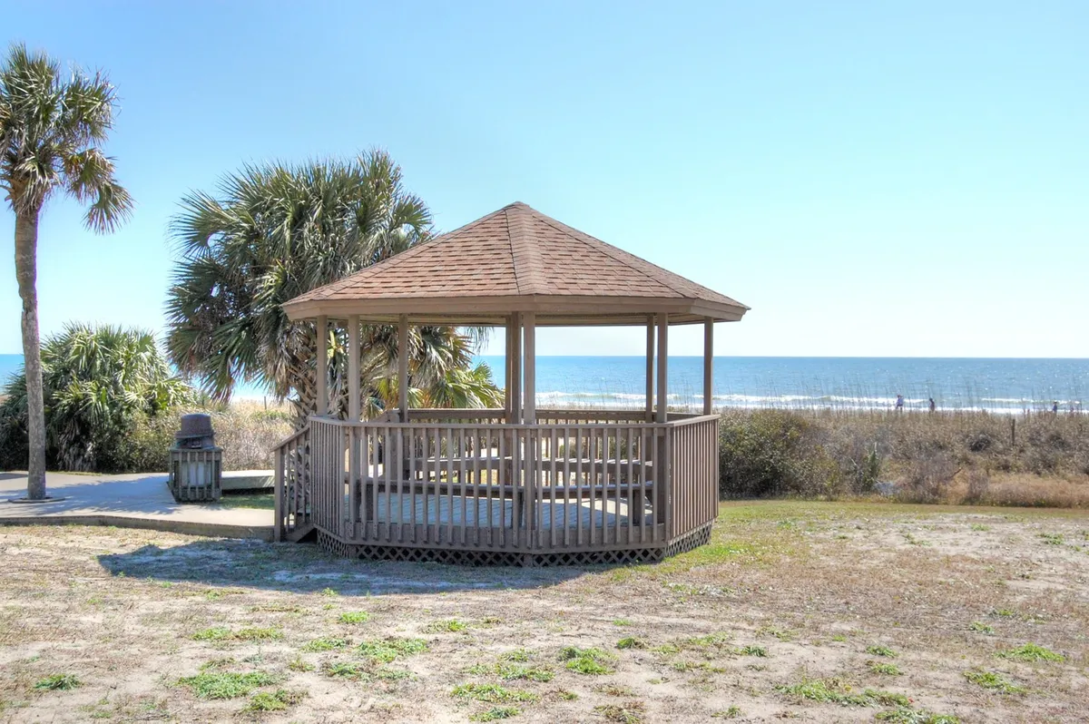 A picturesque beachfront view featuring a gazebo surrounded by palm trees overlooking the ocean. This inviting outdoor space suggests opportunities for relaxing, picnicking, or simply enjoying the coastal scenery.